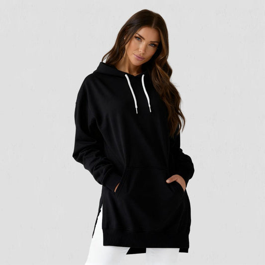 Woman wearing the Junemae oversized hoodie dress in black, with side slits and a kangaroo pocket