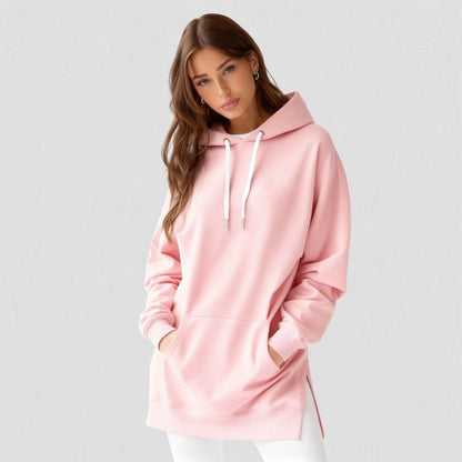 Woman wearing the Junemae oversized hoodie dress in blush pink, with side slits and a kangaroo pocket