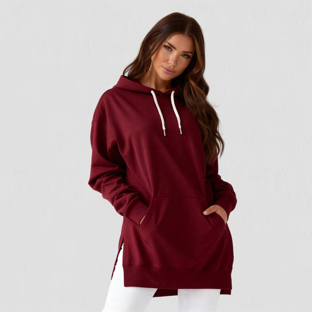 Woman wearing the Junemae oversized hoodie dress in burgundy, with side slits and a kangaroo pocket