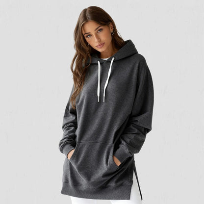 Woman wearing the Junemae oversized hoodie dress in charcoal, with side slits and a kangaroo pocket