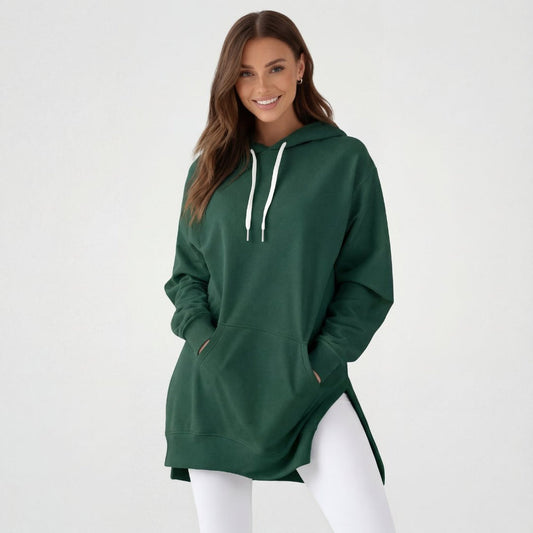 Woman wearing the Junemae oversized hoodie dress in forest green, with side slits and a kangaroo pocket