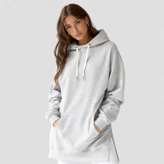 Woman wearing the Junemae oversized hoodie dress in heather grey, with side slits and a kangaroo pocket